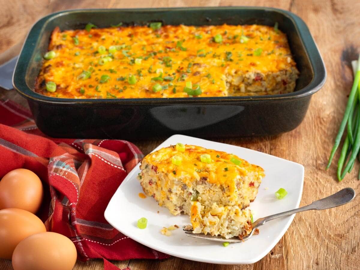 Sausage hashbrown breakfast casserole with a plated serving, eggs, and green onions