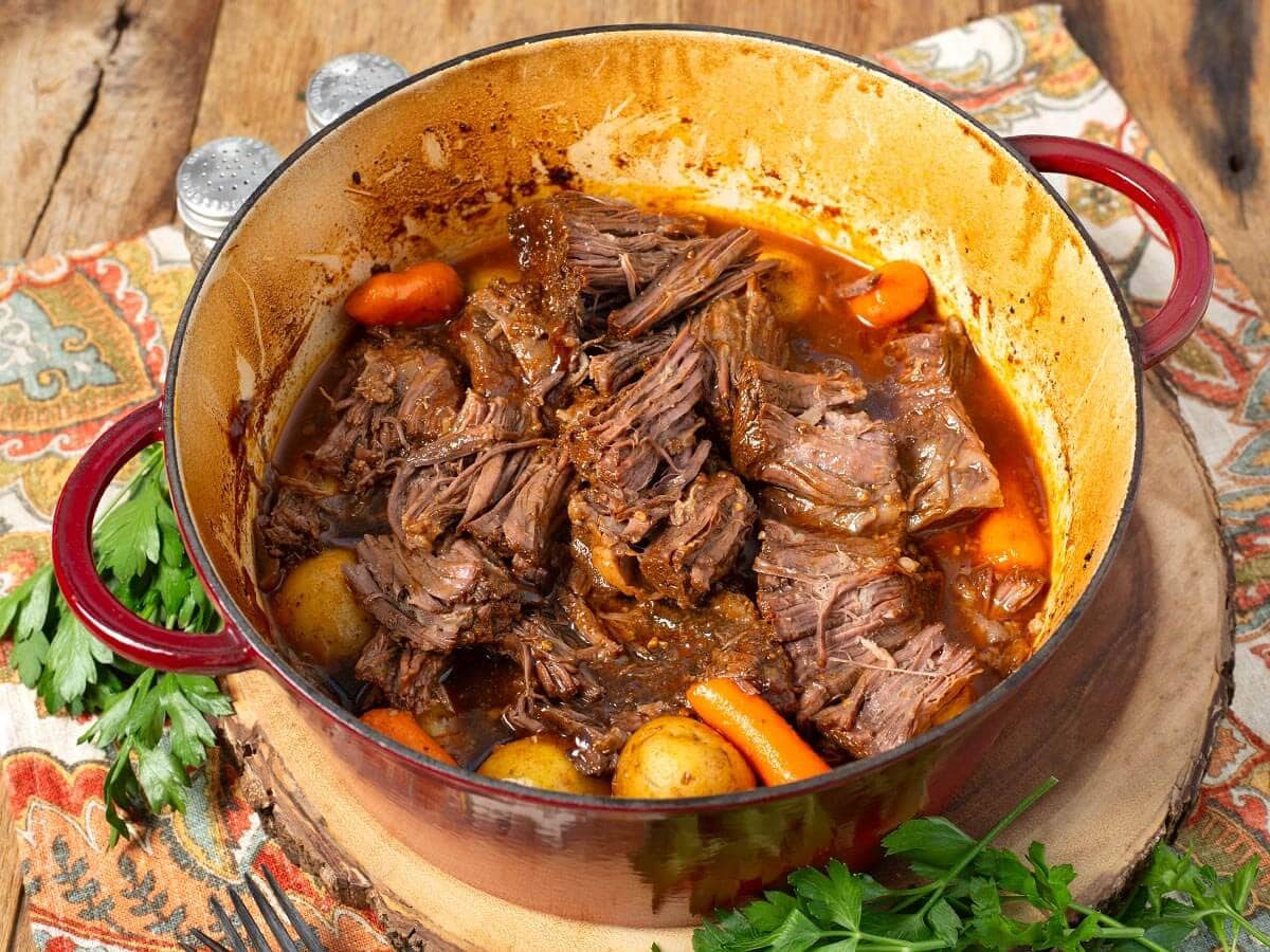 Tender shredded barbecue beef with potatoes and carrots in a red Dutch oven