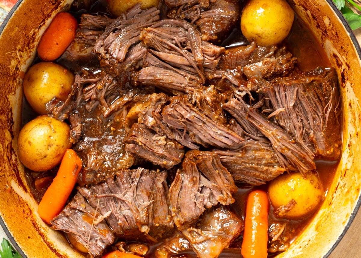Chuck roast, beef broth, soy sauce, onion, garlic, spice rub, liquid smoke, and barbecue sauce on a wooden surface