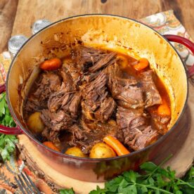 Tender shredded barbecue beef with potatoes and carrots in a red Dutch oven