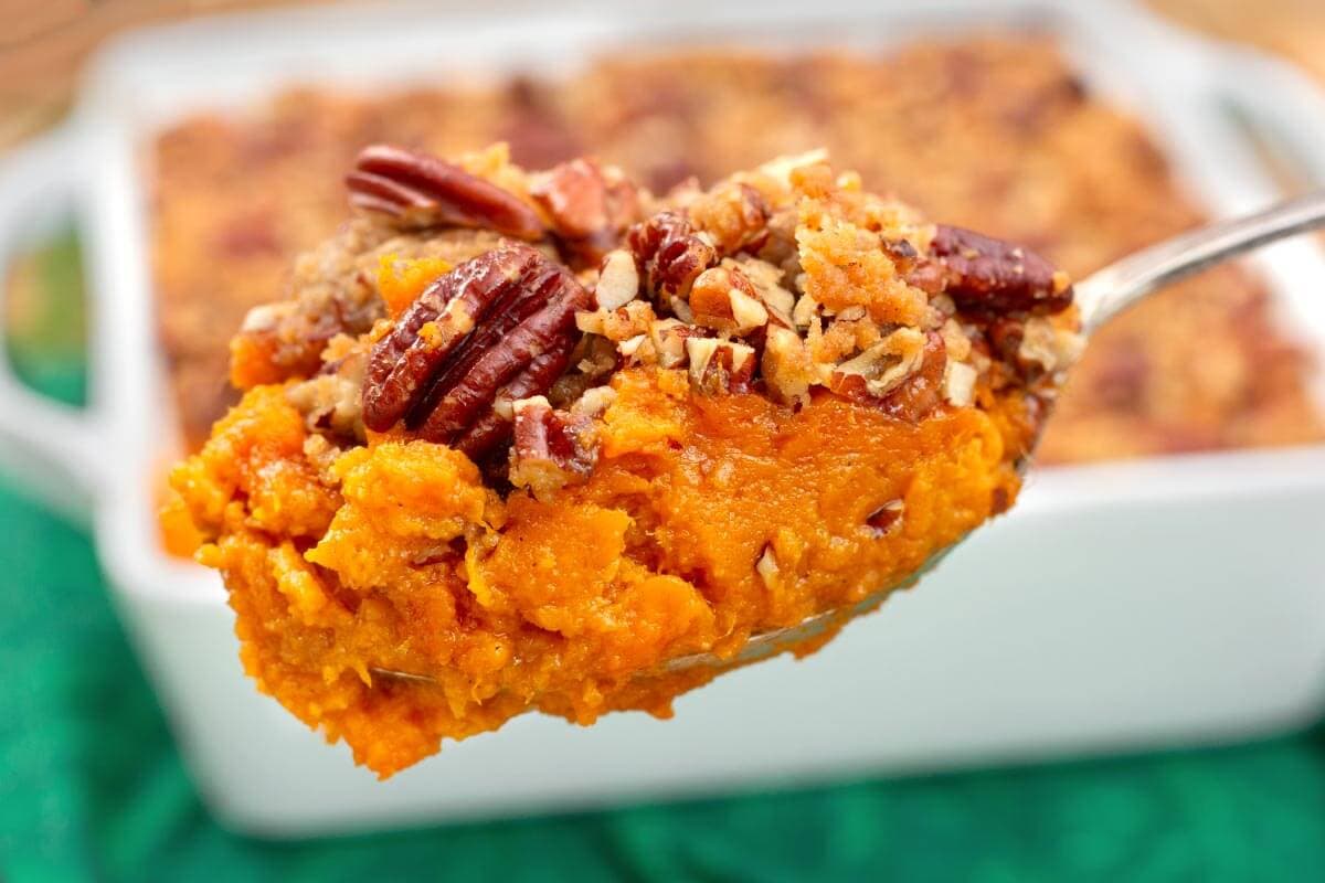 Spoonful of sweet potato casserole with crunchy pecan topping held above a white baking dish