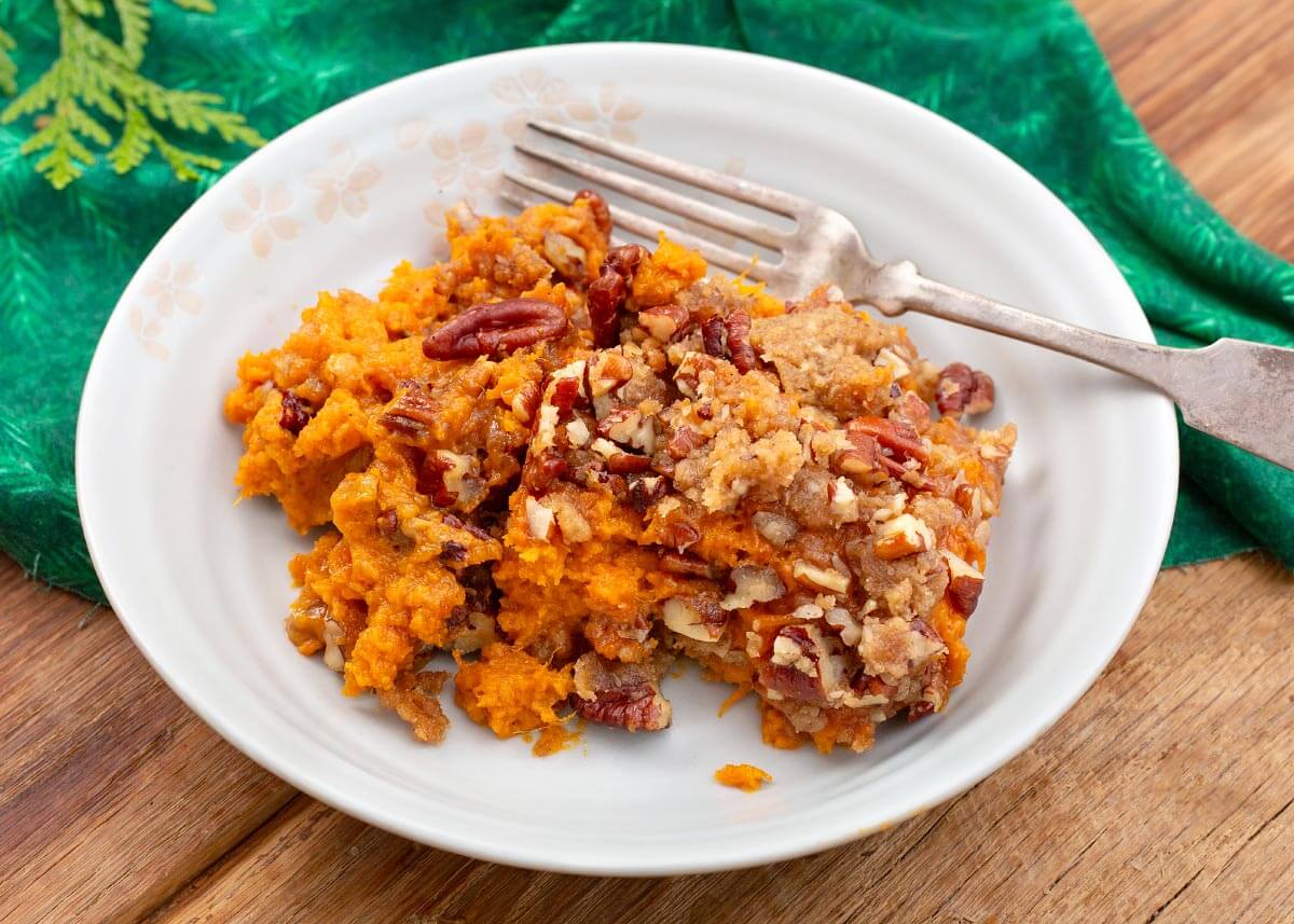 Close-up of sweet potato casserole with brown sugar pecan crumbles on a white plate with a silver fork