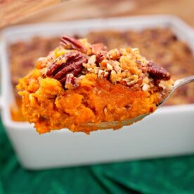 Spoonful of sweet potato casserole with crunchy pecan topping held above a white baking dish